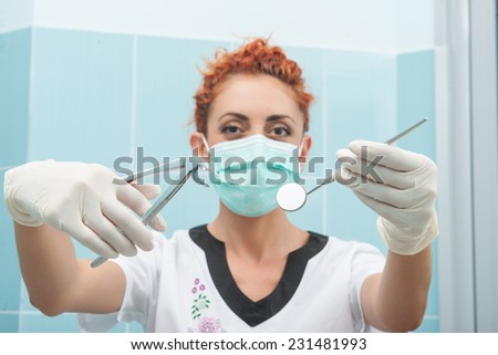 Half-length portrait of young dentist wearing medical mask and gloves standing holding tweezers and little mirror wanted to examine her patient