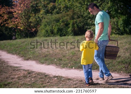 Selective focus on the father and son wearing T-shirts and jeans coming back from the picnic holding a wicker basket