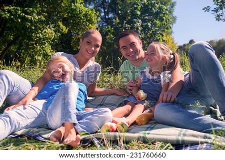 Portrait of happy young family consisted of mom daddy son and little daughter laughing having a picnic