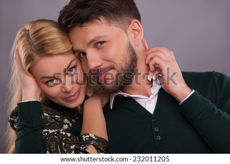 Half-length portrait of beautiful happy couple standing together hugging each other enjoying the moment looking at us. Isolated on dark background