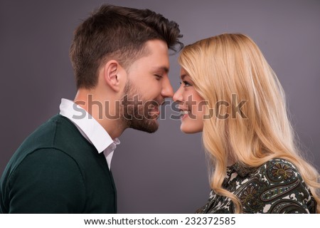 Half-length portrait of lovely happy smiling couple standing facing each other wanted to kiss. Isolated on dark background