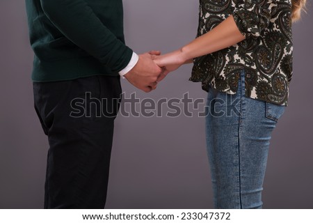 Half-length portrait of young lovely couple standing aside together holding hands. Isolated on dark background