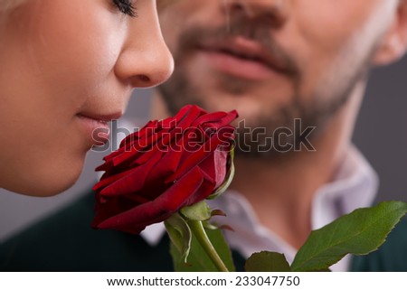 Selective focus on the beautiful young fair-haired woman smelling red rose present from her boyfriend standing on background