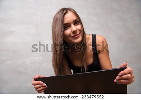 Half-length portrait of sexy young beautiful dark-haired smiling woman wearing nice black top sitting looking at us looking out of her lap top. Isolated on dark background