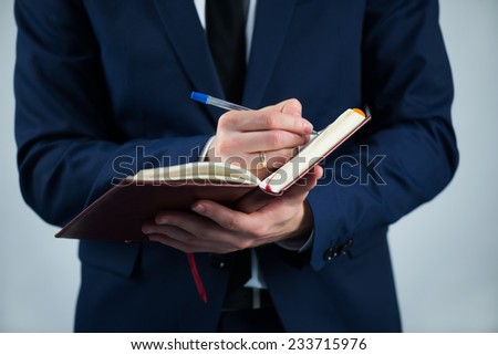 Selective focus on the dairy in the hands of busy man wearing white shirt tie and blue jacket writing something in it