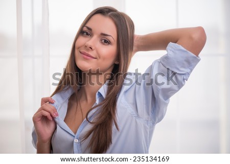 Half-length portrait of dark-haired beautiful smiling girl wearing blue shirt touching it looking at us waking up in the morning