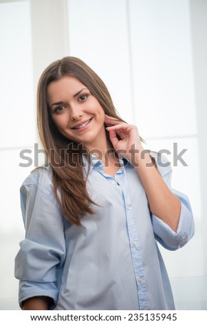 Half-length portrait of dark-haired beautiful smiling girl wearing blue shirt  touching her neck looking at us thinking about wonderful last date