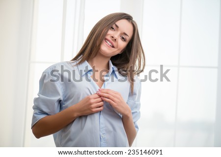 Half-length portrait of dark-haired beautiful smiling girl wearing blue shirt waking up in the morning tacking her blue pajamas looking at us satisfied with her life