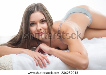 Selective focus on the beautiful dark-haired smiling girl wearing sexy bra lying in the bed looking at us thinking about her future date