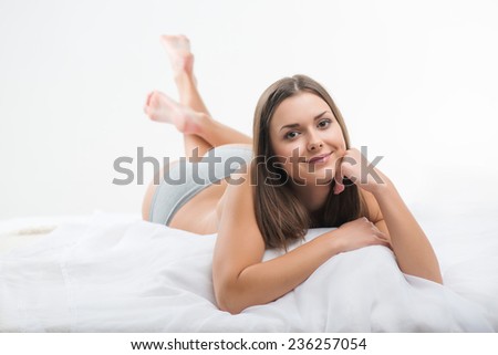 Selective focus on the beautiful dark-haired smiling girl wearing sexy bra lying in the bed looking at us dreaming about her future date