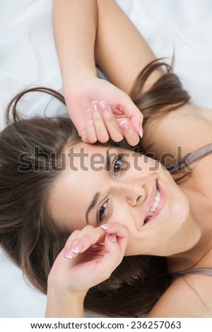 Half-length portrait of dark-haired beautiful smiling girl wearing sexy lingerie lying in the bed waking up in the morning. Top view