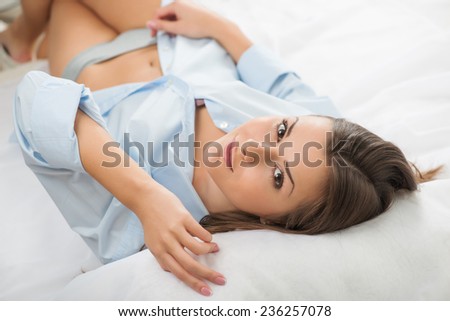 Selective focus on the beautiful dark-haired smiling girl wearing blue pajamas lying in the bed looking at us thinking about miracle evening. Top view