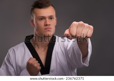 Selective focus on the fist of young handsome fair-haired karate enthusiast wearing white kimono coaching himself before the important fight