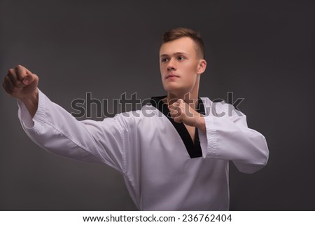 Half-length portrait of young handsome fair-haired karate enthusiast wearing white kimono coaching himself before the important fight. Isolated on the dark background