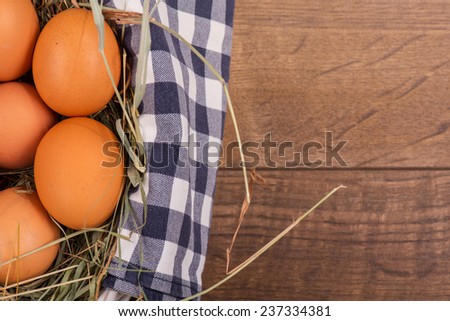 Wonderful basket with the straw and eggs inside standing on the wooden table. Top view