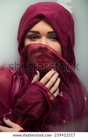 Half-length portrait of beautiful sexy dark-haired woman lying in the bath covering herself with the wine-colored cloth looking at us seductively. Top view