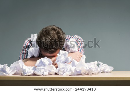 In search of inspiration. Close-up of author lying in the heap of crumpled paper while sitting against grey background