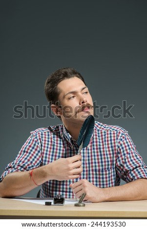 Writing with feather pen. Close-up of man writing with feather pen and inkbottle while sitting against grey background