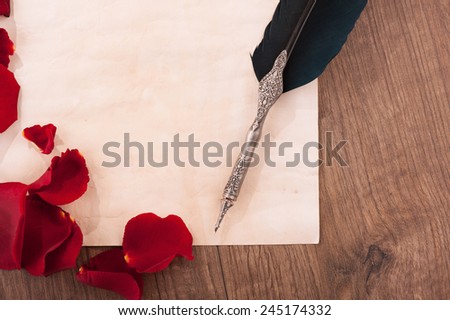 Love letter. Closeup image of vintage paper with copy space and feather pen arranged on wooden table and decorated with rose petals