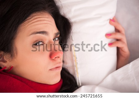 Take a sick day. Closeup image of young sick woman lying in bed with sore throat in scarf and looking at camera