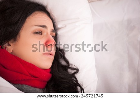 Not feeling too great. Closeup image of young sick woman lying in bed with red nose in thick scarf and looking away in frustration at copy space