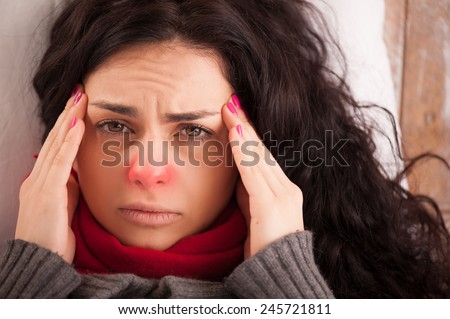 Flu or cold. Closeup top view image of frustrated young woman with red nose and suffering from terrible headache while lying in bed