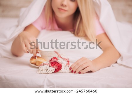 Breakfast in bed. Closeup image of young woman covered with blanket having french breakfast with coffee and croissants served to bed due to valentines day, selective focus on rustic gift hearts