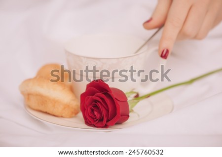 Morning coffee. Closeup image of red rose in selective focus and a cup of coffee with croissant