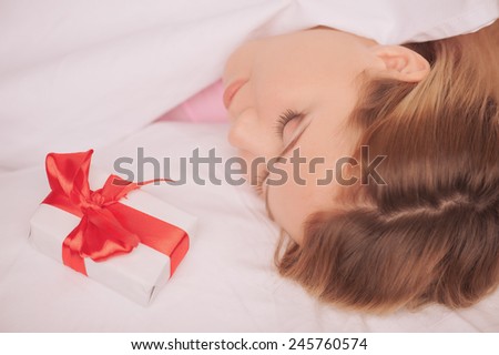 What a beautiful morning. Top view portrait of young beauty sleeping while a gift box with red ribbon is placed on her pillow