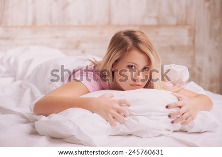 Insomnia. Young beautiful thoughtful woman hugging pillow and looking sad while lying in bed on country house background
