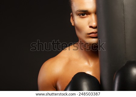No losers here. Handsome African sportsman looking at camera during workout while standing by the punching bag on dark background