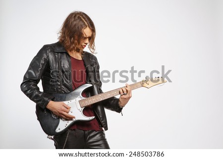 Creative soul. Handsome young man in leather jacket playing the guitar while standing on grey background