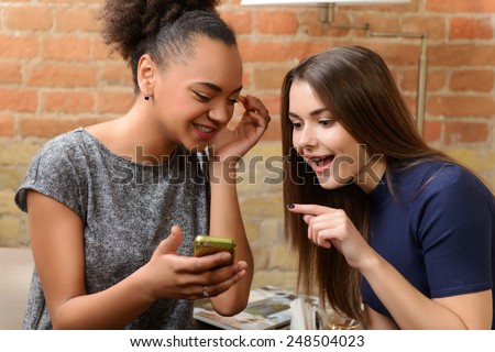 Happy friends in restaurant. Two young women having fun and watching photos on cell phone while drinking coffee at the restaurant