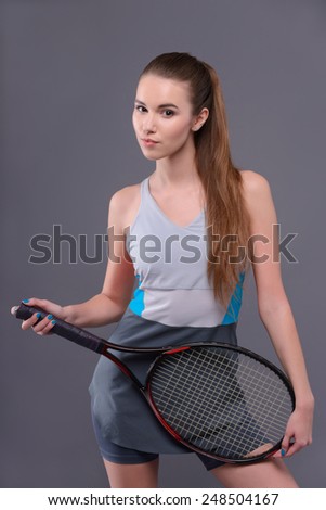 Are you ready to play. Portrait of beautiful young woman in sports clothing holding tennis racket and smiling while standing isolated over the grey background
