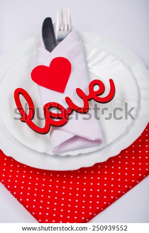 Serving up a little romance. Top view closeup of romantic dinner cutlery with red heart and love lettering decorations on the white plate