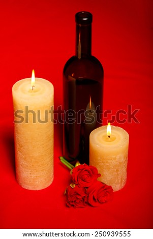 On a romantic date. Top view closeup of romantic burning candles with a bottle of wine and roses placed on a red canvas