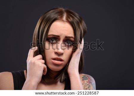 Feeling hopeless. Young trapped woman with tattoo holding head in hands while sitting in a dark room