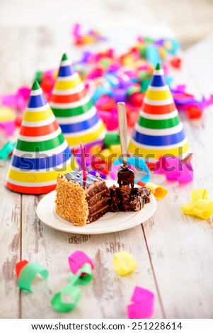 It is a special day. Image of a delicious chocolate cake with a candle and fork surrounded by party hats and confetti on the background