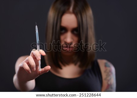 Escaping from reality. Selective focus image of young woman showing a heroin injection in syringe while standing on dark background