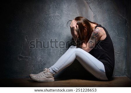 Feeling hopeless. Young woman trapped holding head in hands while sitting on the floor in a dark room