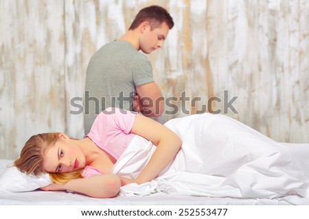 Not seeing eye to eye. Side view of a young couple having a disagreement while woman lying in bed and man sitting on the background