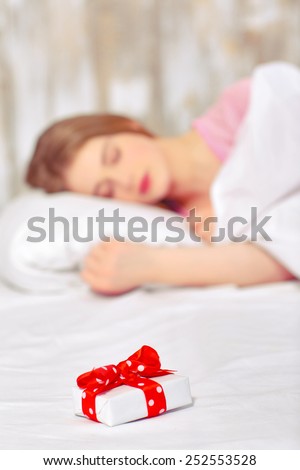 Happy birthday. Portrait of a beautiful young woman sleeping in bed having a birthday gift on her pillow with selective focus