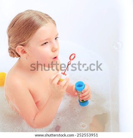 Happy days of childhood. Top view image of a cute little girl taking a bath and playing with soap bubbles while sitting in a luxurious bathtub