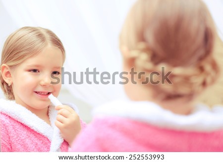 Pretty like my mother. Closeup image of a cute little girl in a pink bathrobe using lipstick while looking at her reflection in the mirror