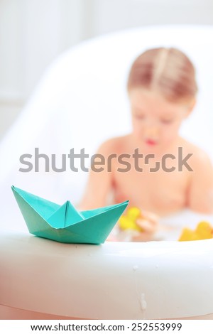 Bath time is fun. Selective focus image of a cute little girl taking a bath and playing with rubber ducks and paper ships while sitting in a luxurious bathtub