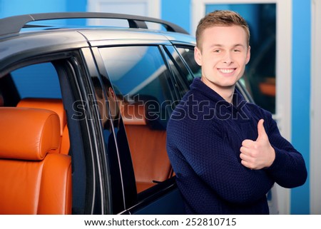 It is the best car ever. Portrait of a handsome smiling man standing by his luxury car in the garage and showing his thumb up
