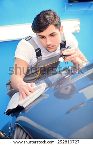 Checking his ideal work. Portrait of a handsome car mechanic polishing the luxury car with wiper and lighter in car repair shop