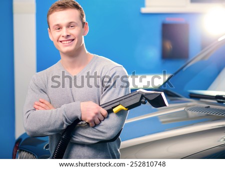 Normal Saturday of car owner. Closeup of handsome smiling young man standing by his luxury car with his hands crossed while holding a car vacuum cleaner car service