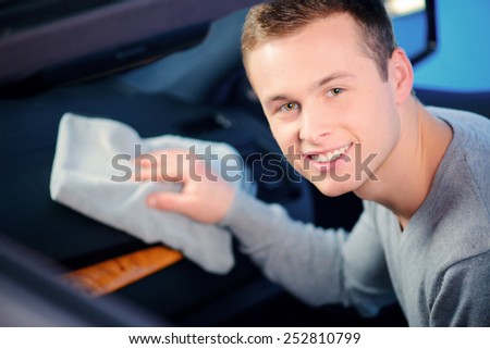 Cleaning his car. Top view of handsome smiling young man cleaning his car dash board with a wiper in selective focus