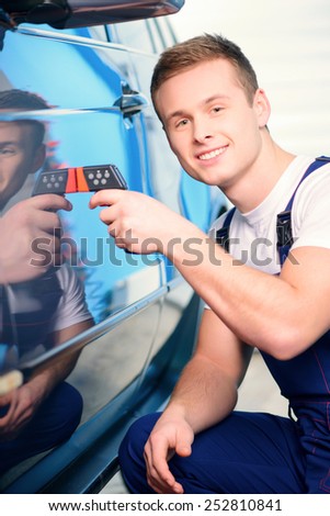 Measuring coating thickness. Closeup of a handsome car mechanic checking the thickness of car coating with a special electronic tool in car repair station
